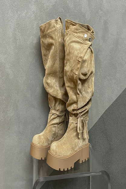 Pair of beige suede platform boots on a clear stand against a gray background