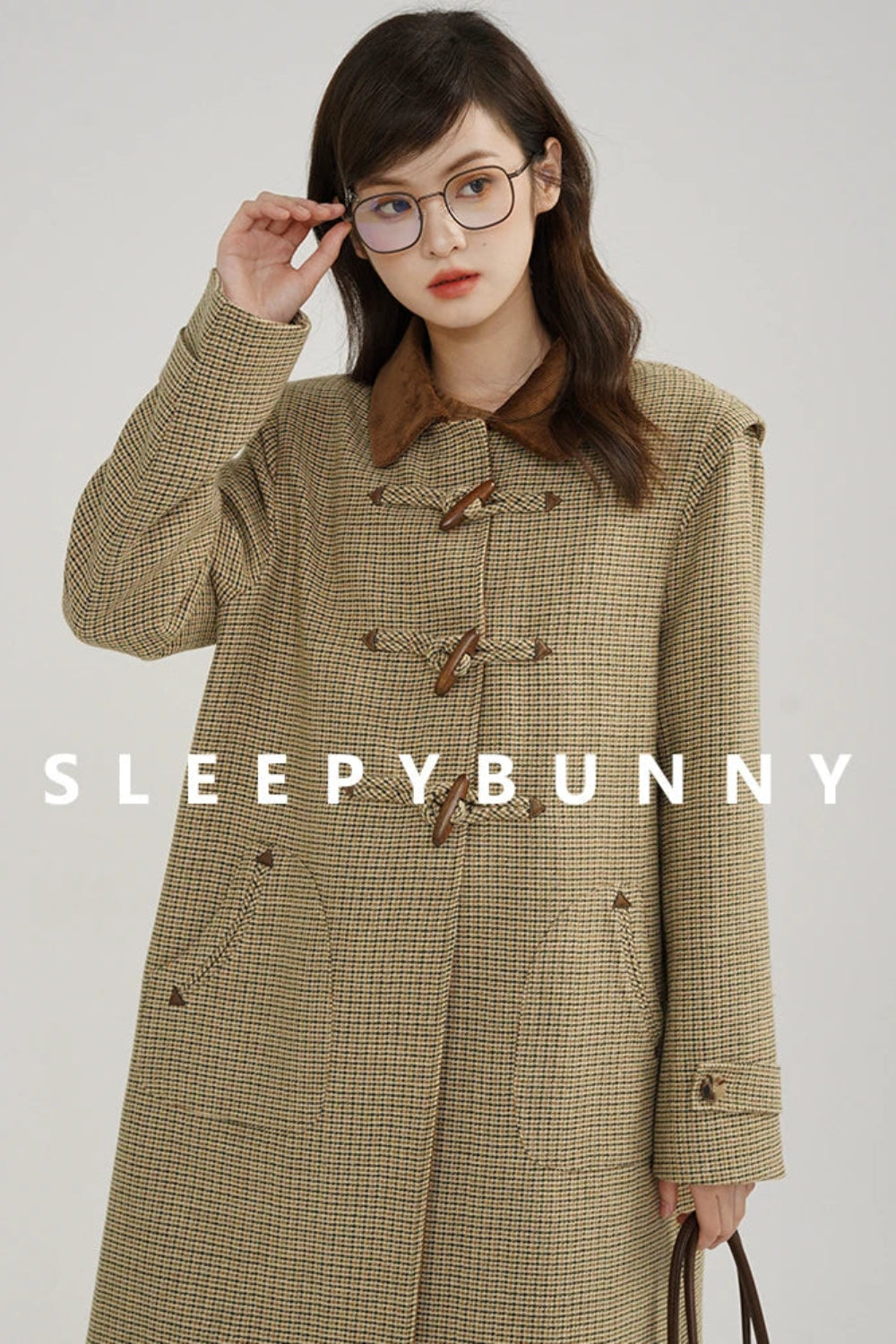 Woman wearing a plaid coat with 'Sleepy Bunny' branding on a gray background