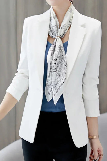 Person wearing a white blazer with a patterned scarf and holding a black handbag.