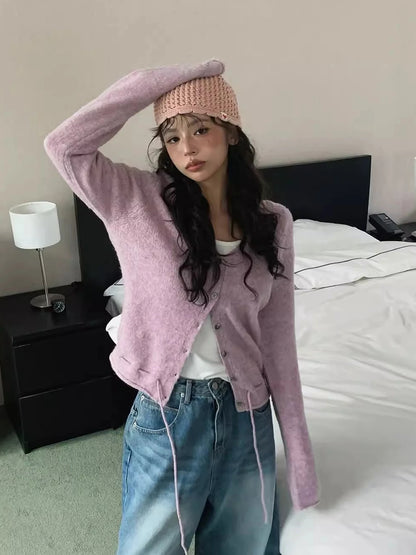 Person wearing a pink cardigan, white shirt, and blue jeans in a bedroom setting.