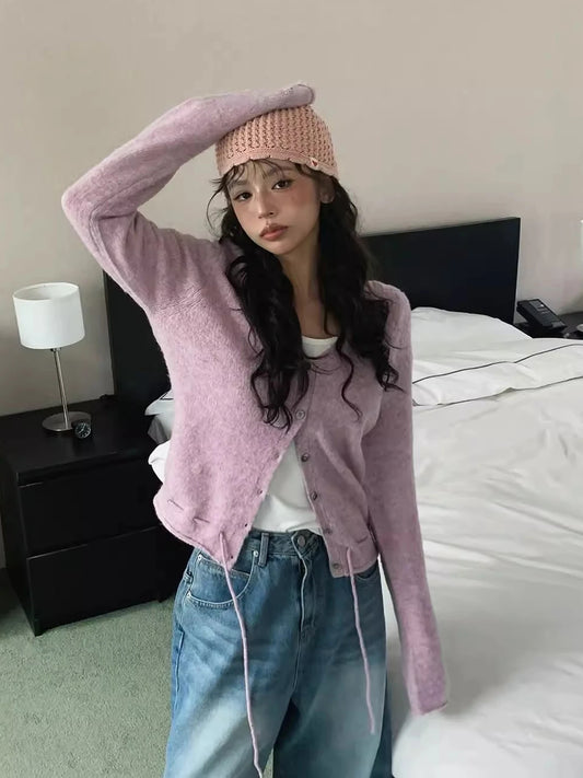 Person wearing a pink cardigan, white shirt, and blue jeans in a bedroom setting.