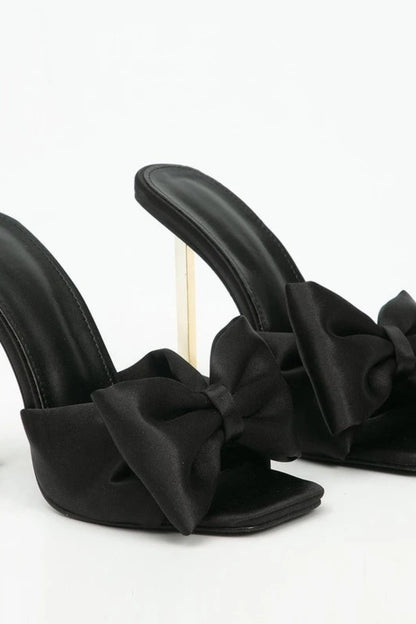 Black high-heeled shoes with bow details on a white background