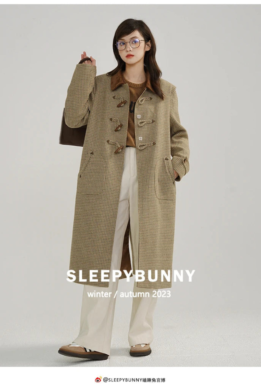 Woman wearing a long beige coat with 'Sleepy Bunny' branding on a gray background
