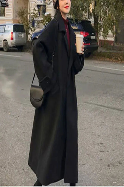 Person wearing a long black coat on a street.