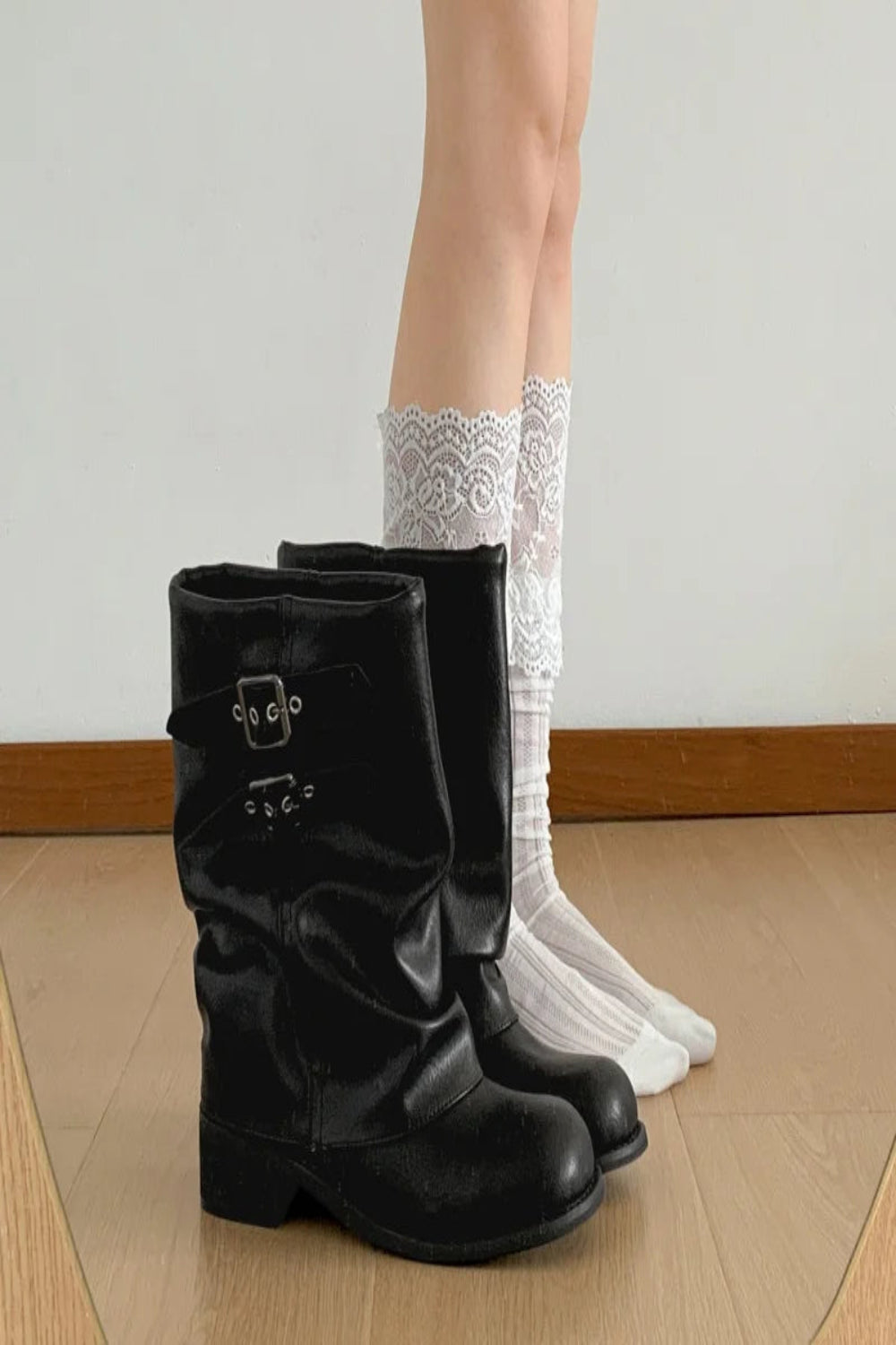Black boots worn with white lace socks on a wooden floor.