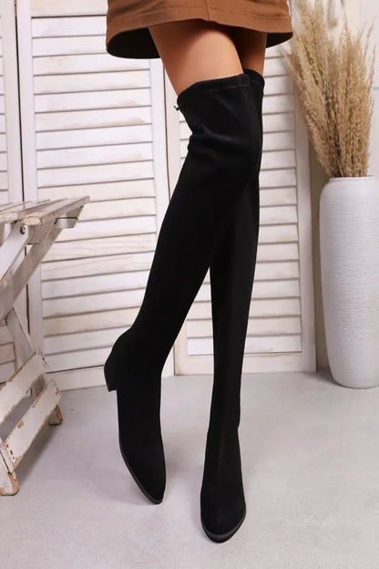 Black knee-high boots worn with a brown skirt against a white background