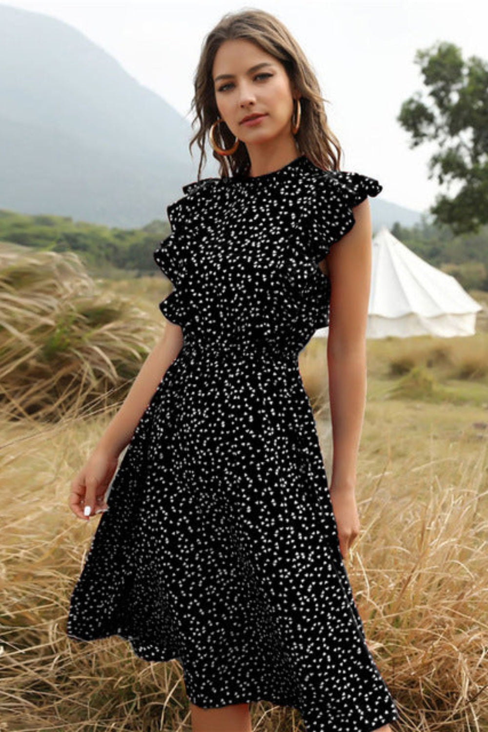 Woman in a black floral dress standing in a field with a tent in the background