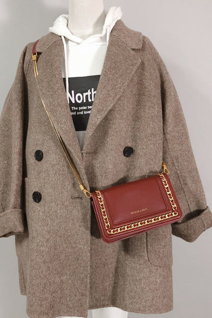 Mannequin wearing a brown coat with a red handbag on a plain background