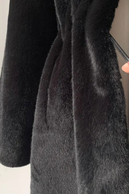 Close-up of a black coat with a hand adjusting the collar against a neutral background