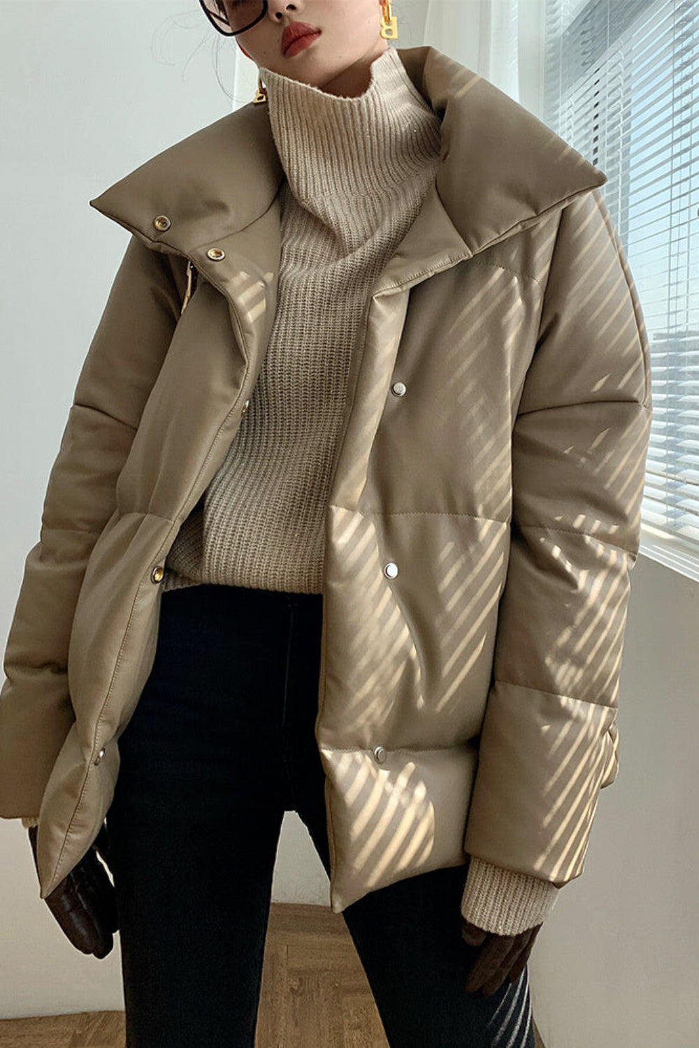 Person wearing a beige puffer jacket over a beige turtleneck sweater indoors.
