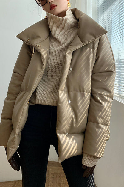 Person wearing a beige puffer jacket over a beige turtleneck sweater indoors.