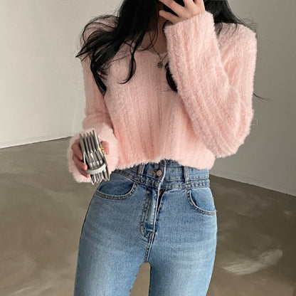 Person wearing a pink fuzzy sweater and blue jeans, holding a phone with a blurred background.