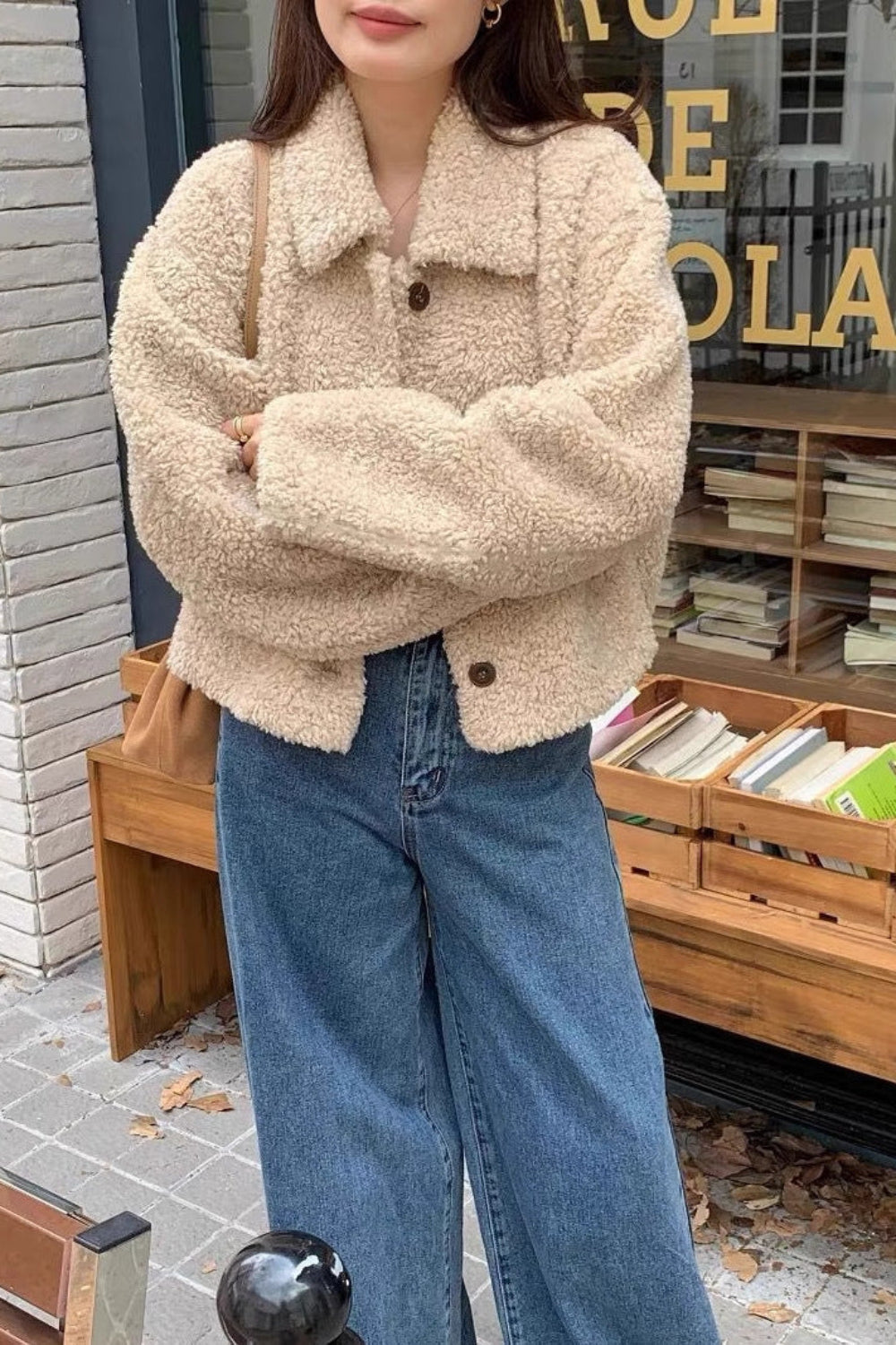 Person wearing a beige sherpa jacket and blue jeans standing in front of a store with books.