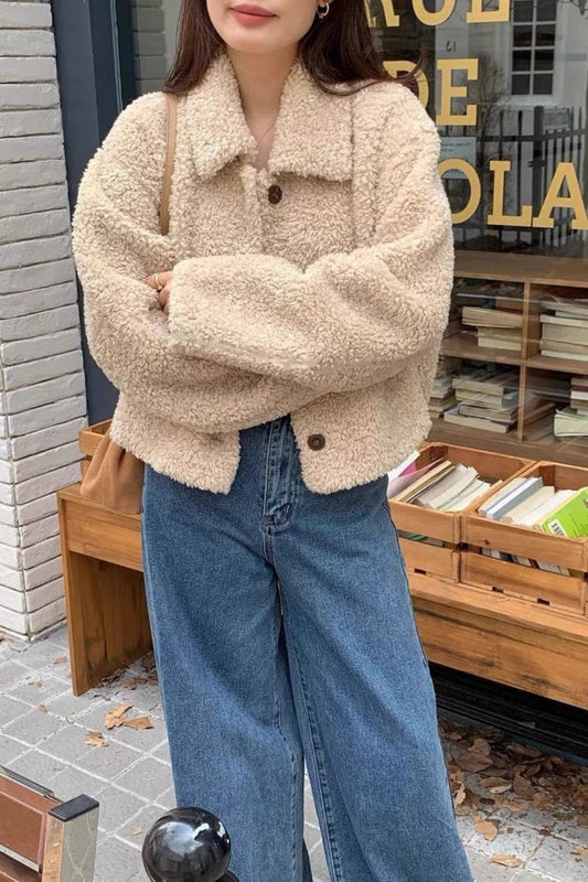 Person wearing a beige sherpa jacket and blue jeans standing in front of a store with books.