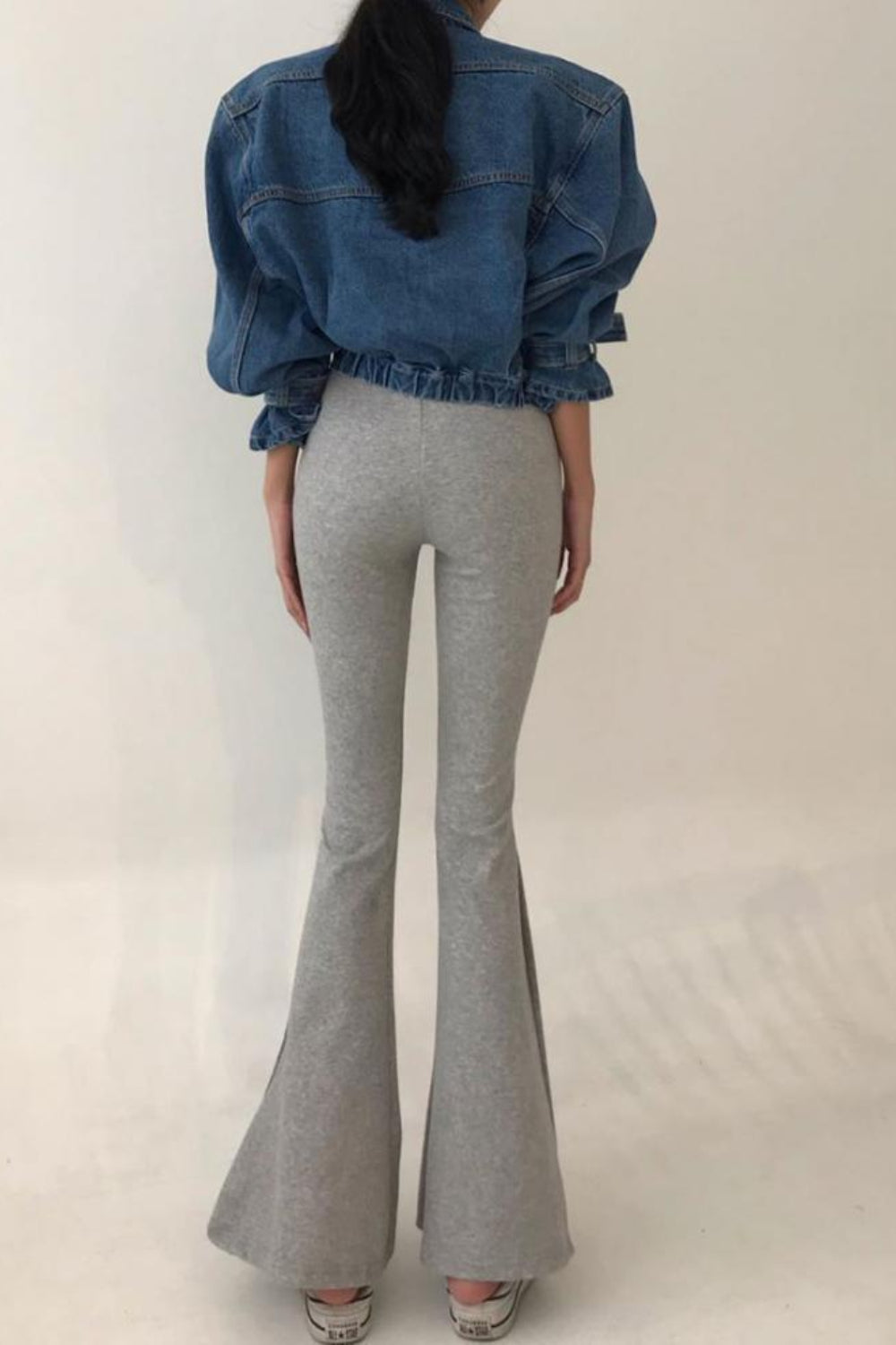 Person wearing a blue denim jacket and gray flared pants on a plain background