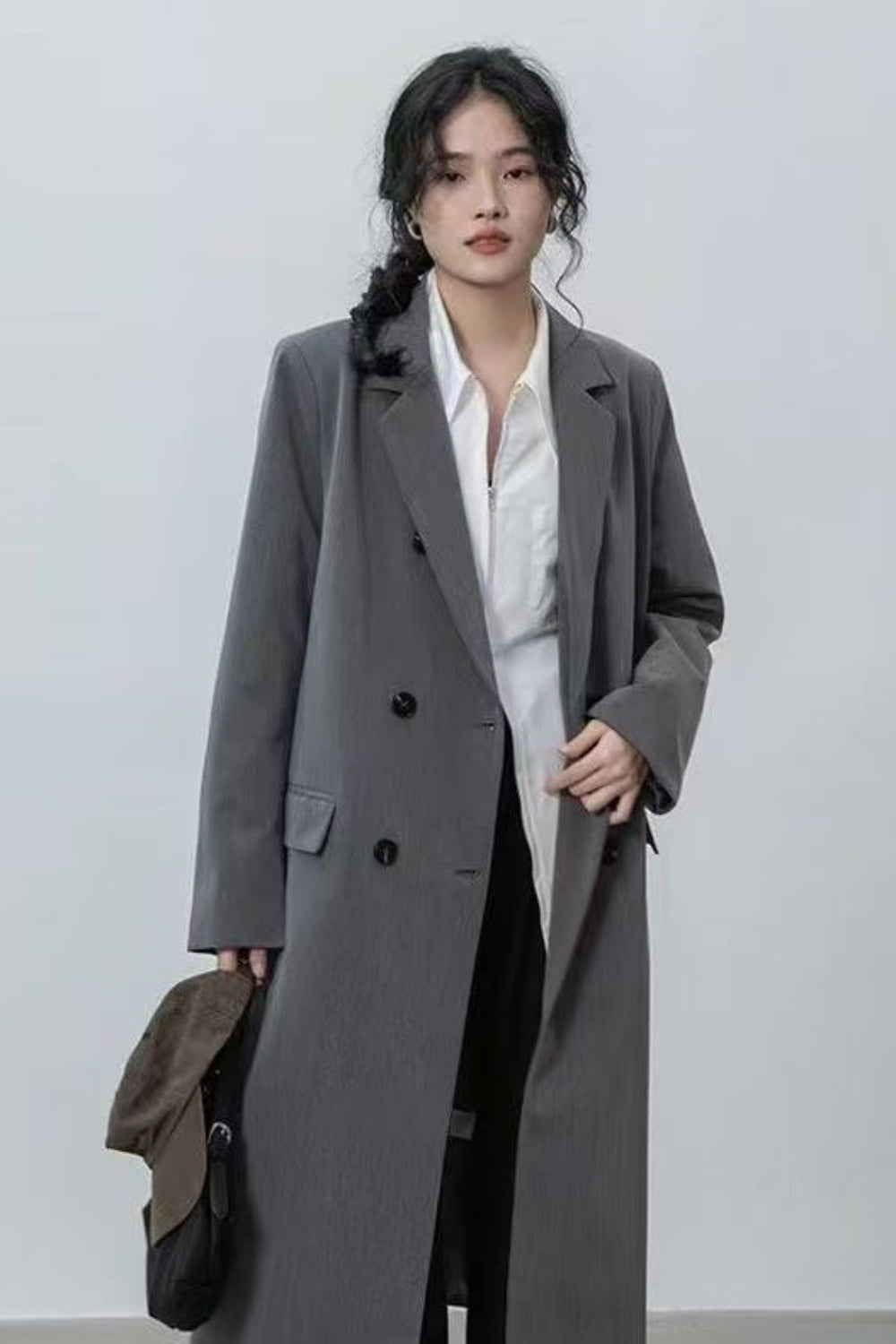 Woman wearing a long gray coat over a white shirt on a plain background