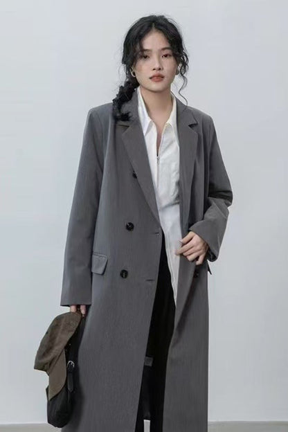 Woman wearing a long gray coat over a white shirt on a plain background