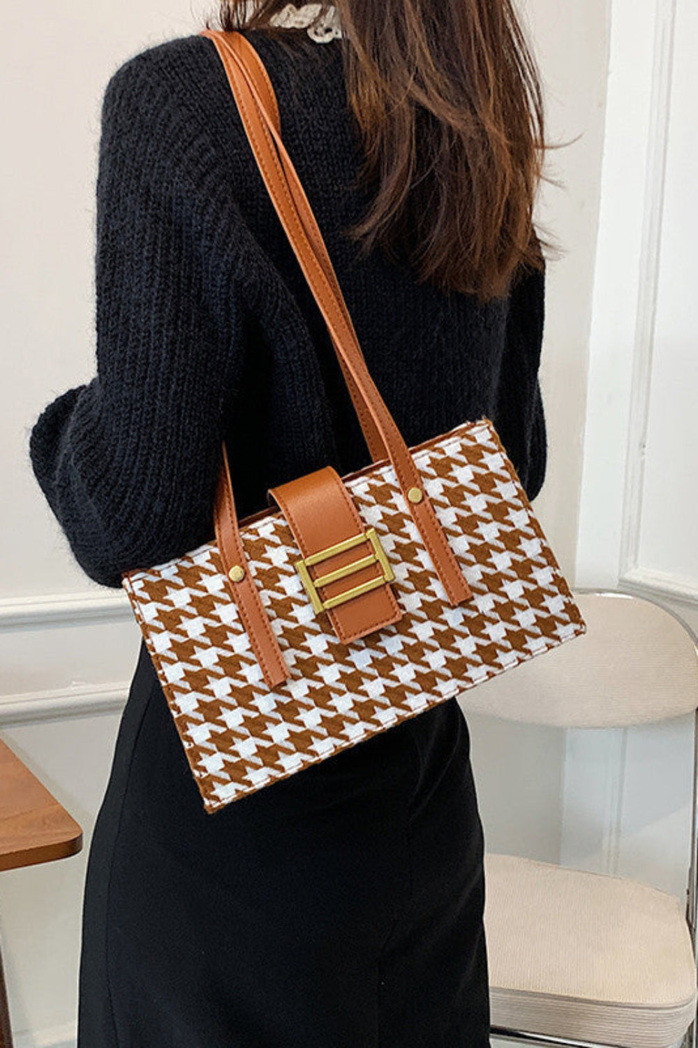 Person holding a brown and white patterned handbag in an indoor setting