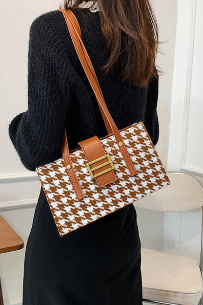 Person holding a brown and white patterned handbag in an indoor setting