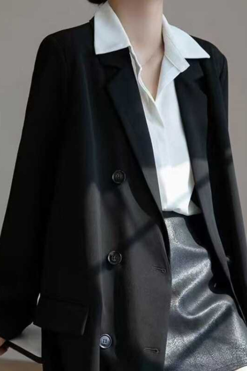 Person wearing a black blazer over a white shirt with a gray background