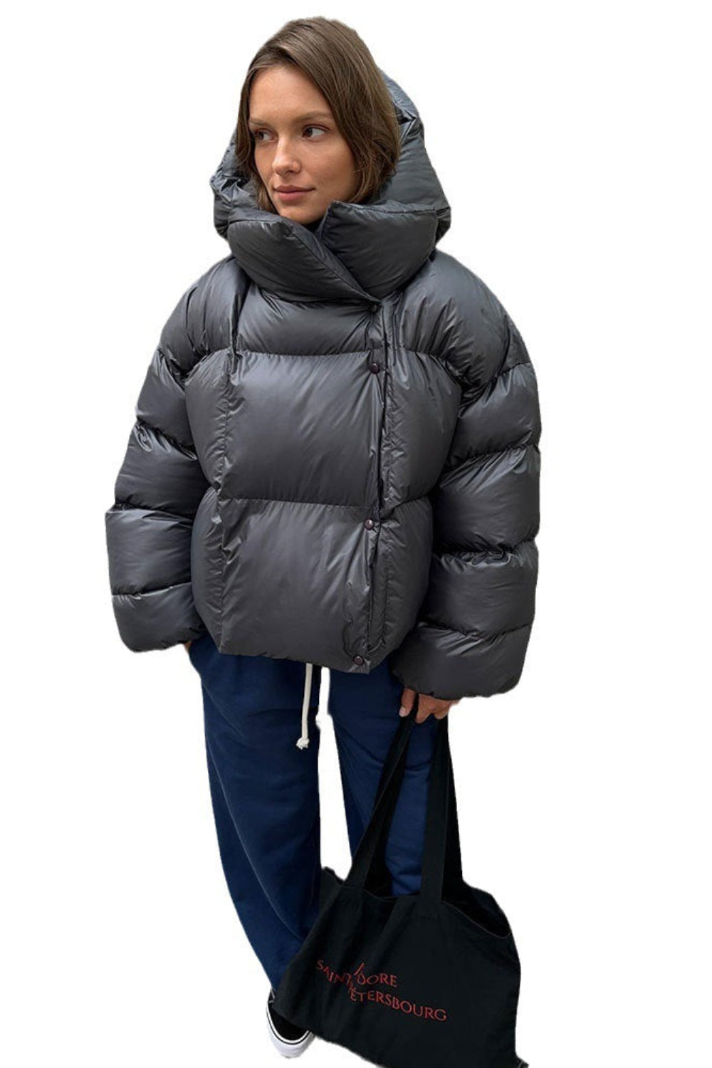 Person wearing a gray puffer jacket holding a black bag on a white background