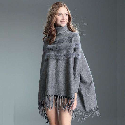 Woman wearing a gray poncho with fringe details on a gray background