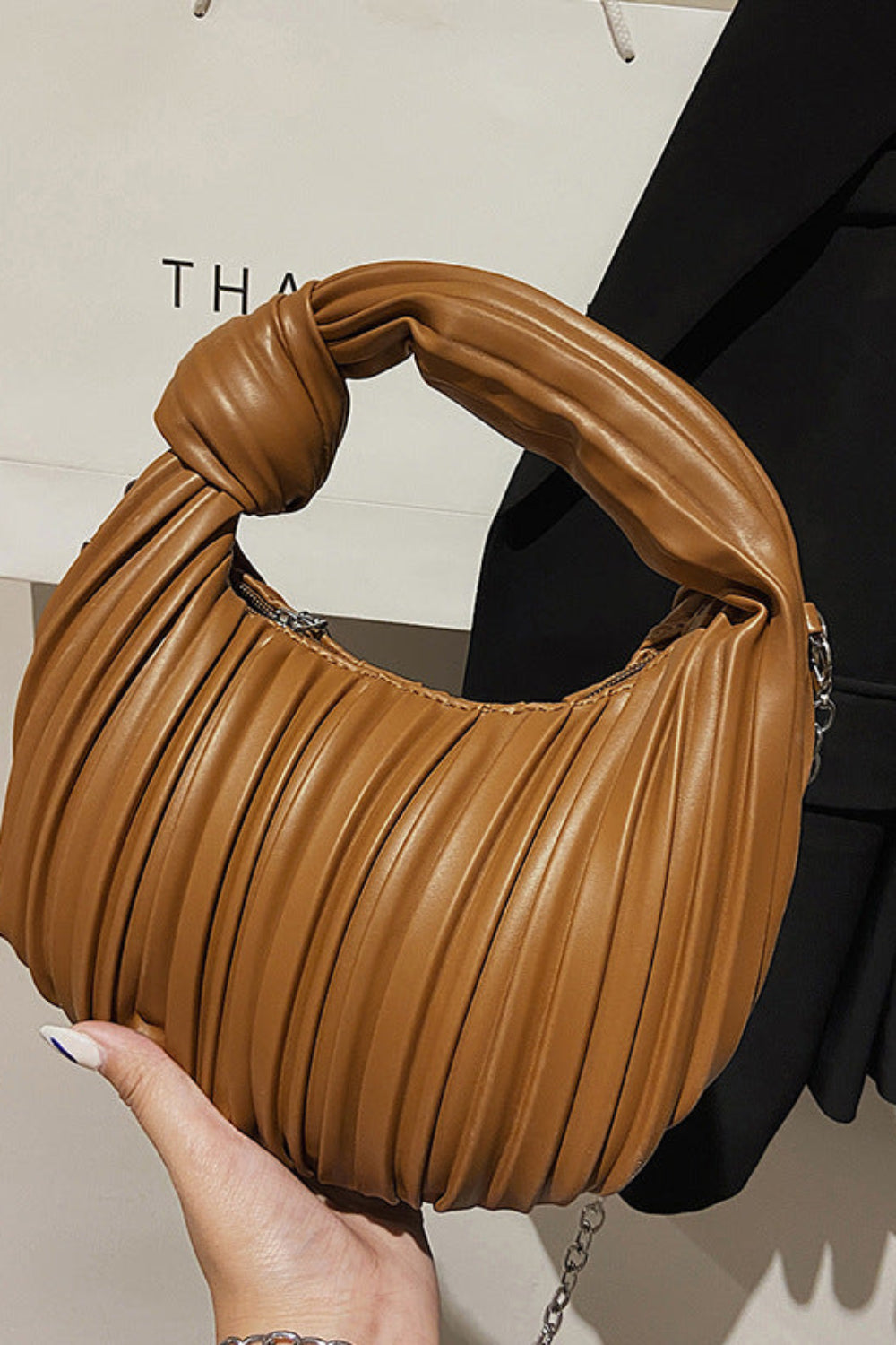 Brown pleated handbag held by a hand with a blurred background