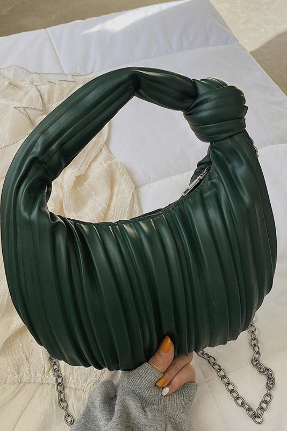 Green pleated handbag with a chain detail held by a hand on a light-colored surface.