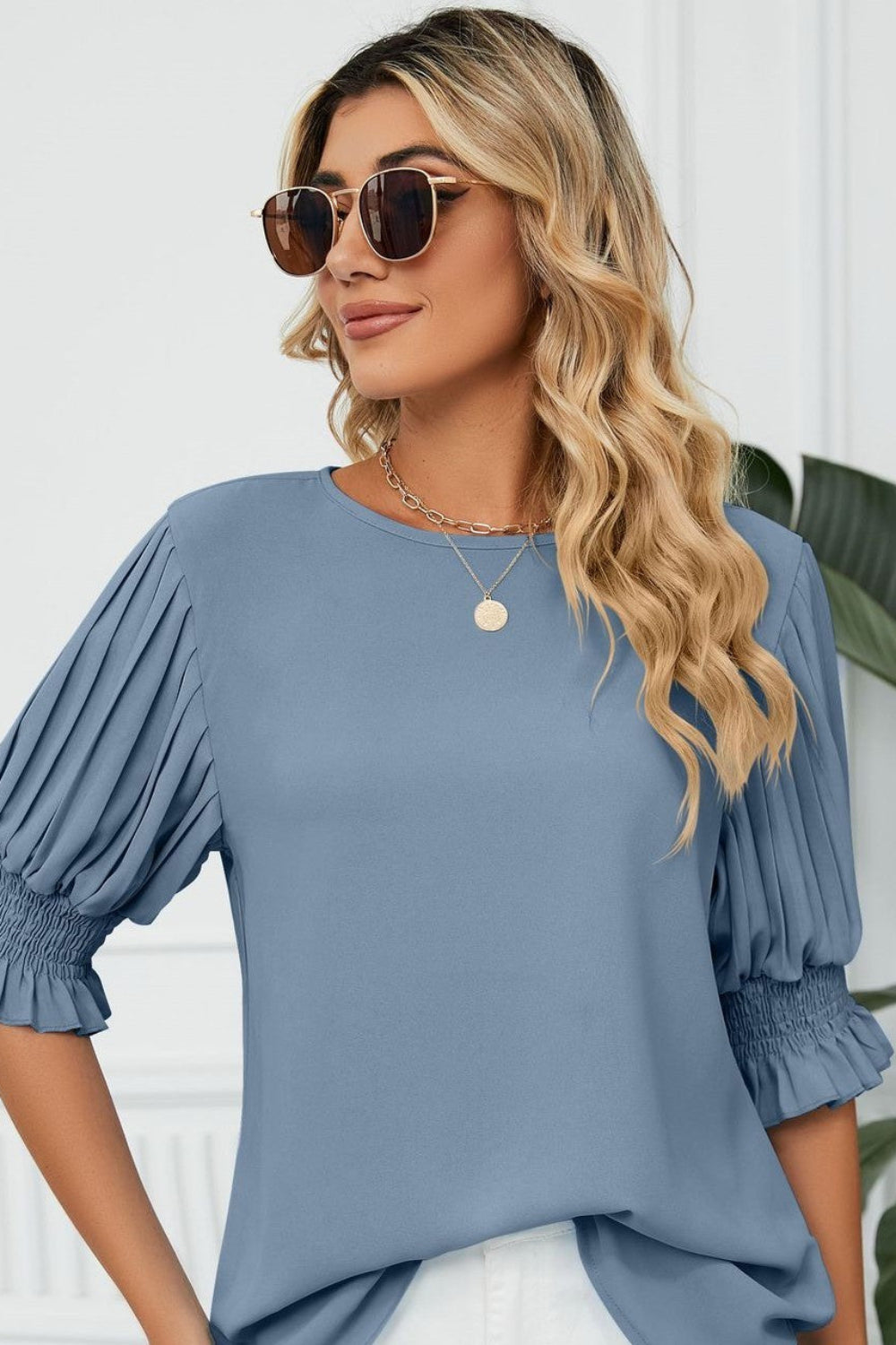 Woman wearing a blue blouse with puffed sleeves against a white wall.