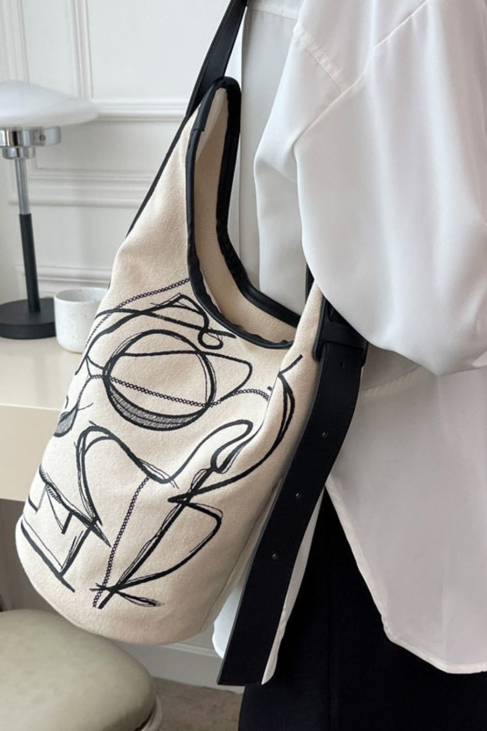 Person holding a tote bag with black abstract design in a room setting