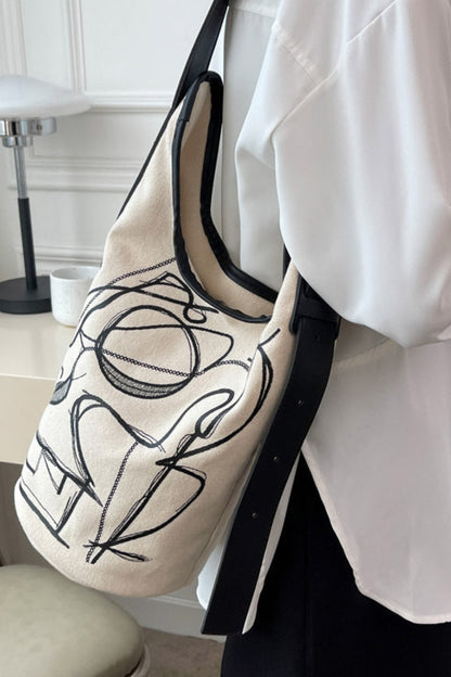 Person holding a tote bag with black abstract design in a room setting