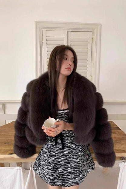 Woman wearing a fur coat in a room with a wooden table and white walls.