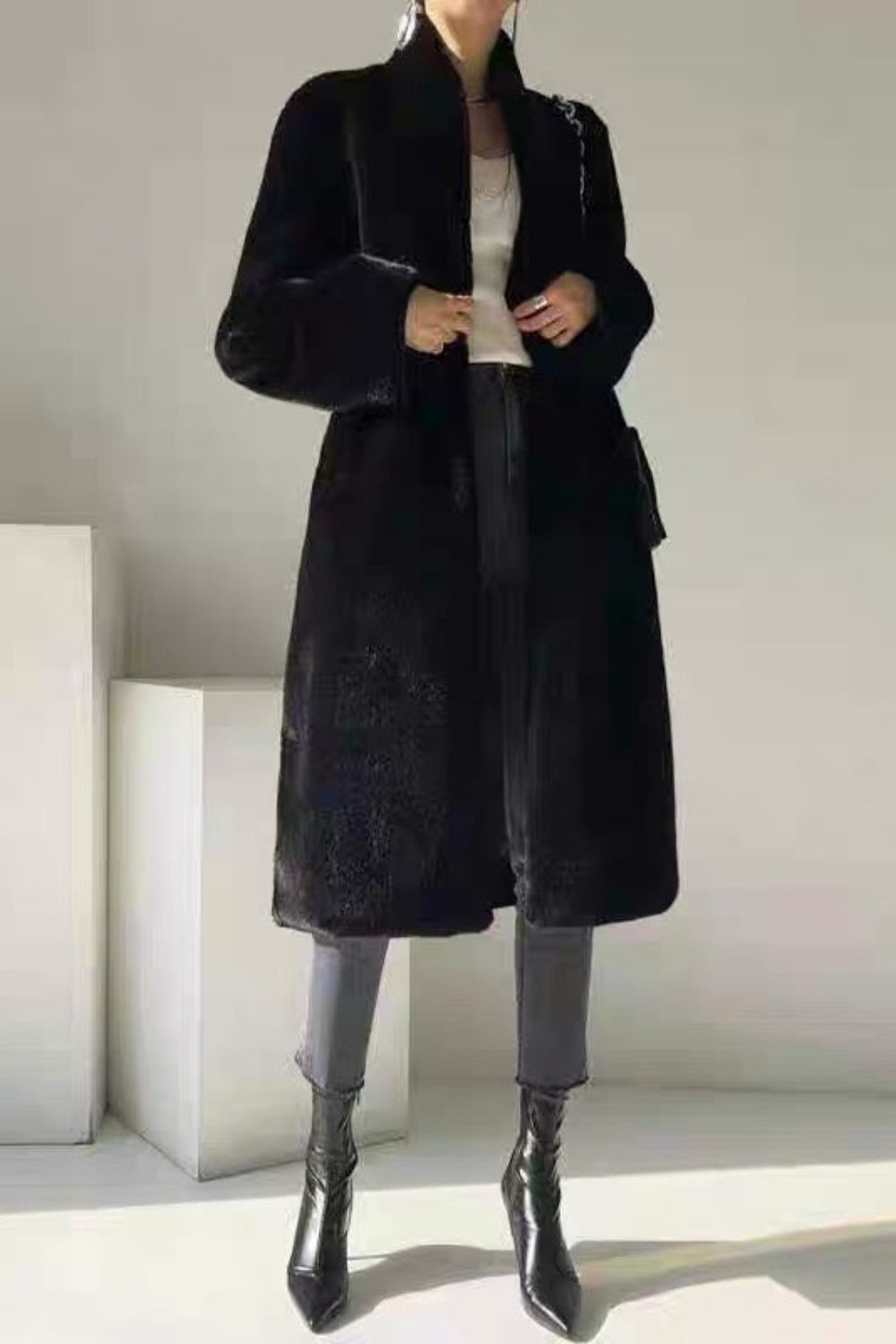 Person wearing a black coat in a minimalistic setting