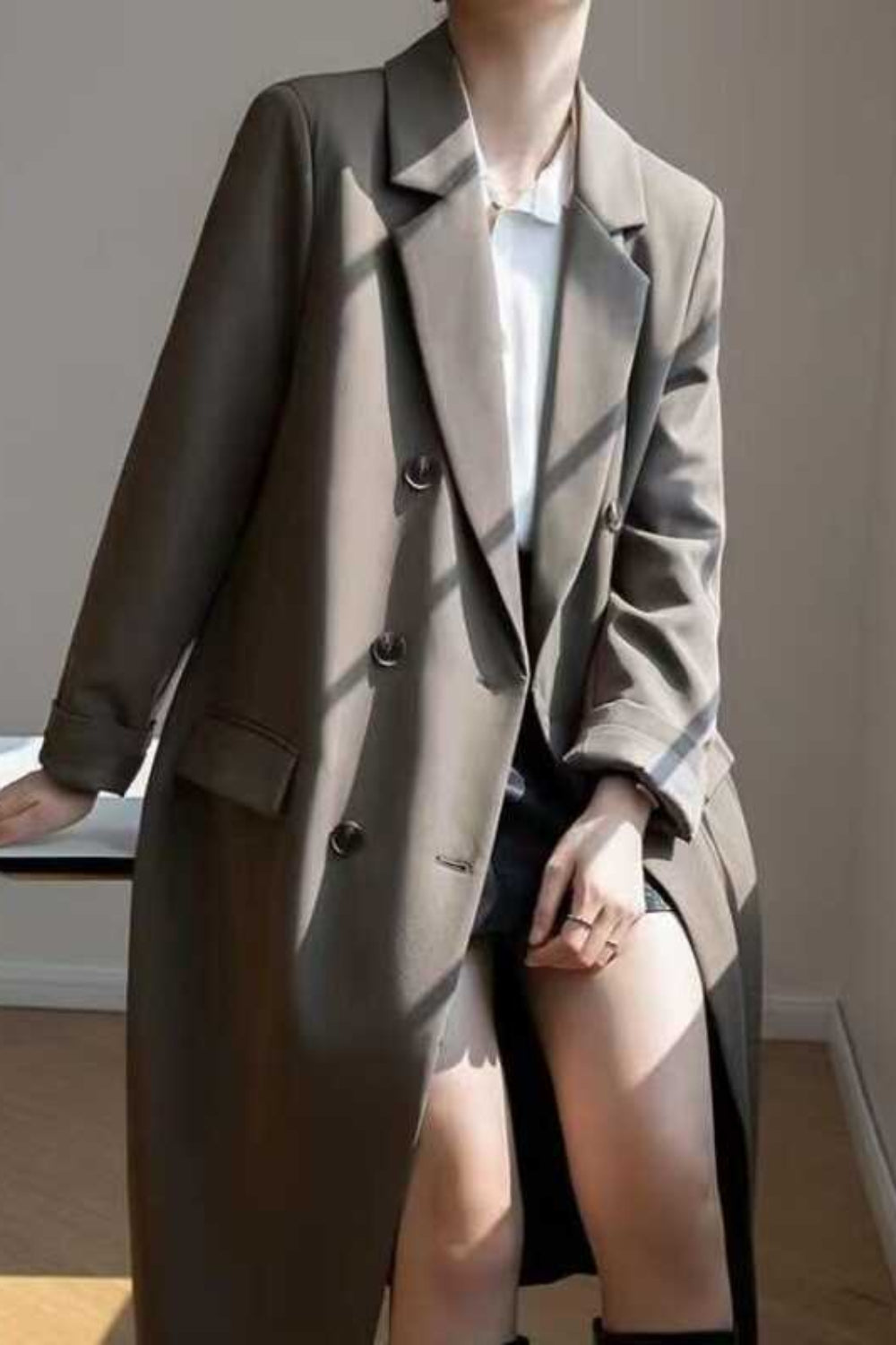 Person wearing a long coat in a room with a window