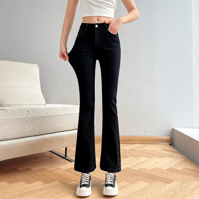 Person wearing black flared jeans in a room with a light gray wall and beige sofa.