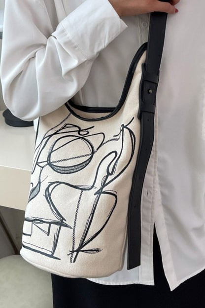 Person holding a beige tote bag with black abstract designs in an indoor setting.