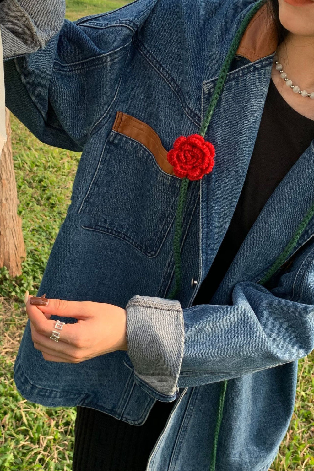 Person wearing a blue denim jacket with a red flower accessory outdoors.