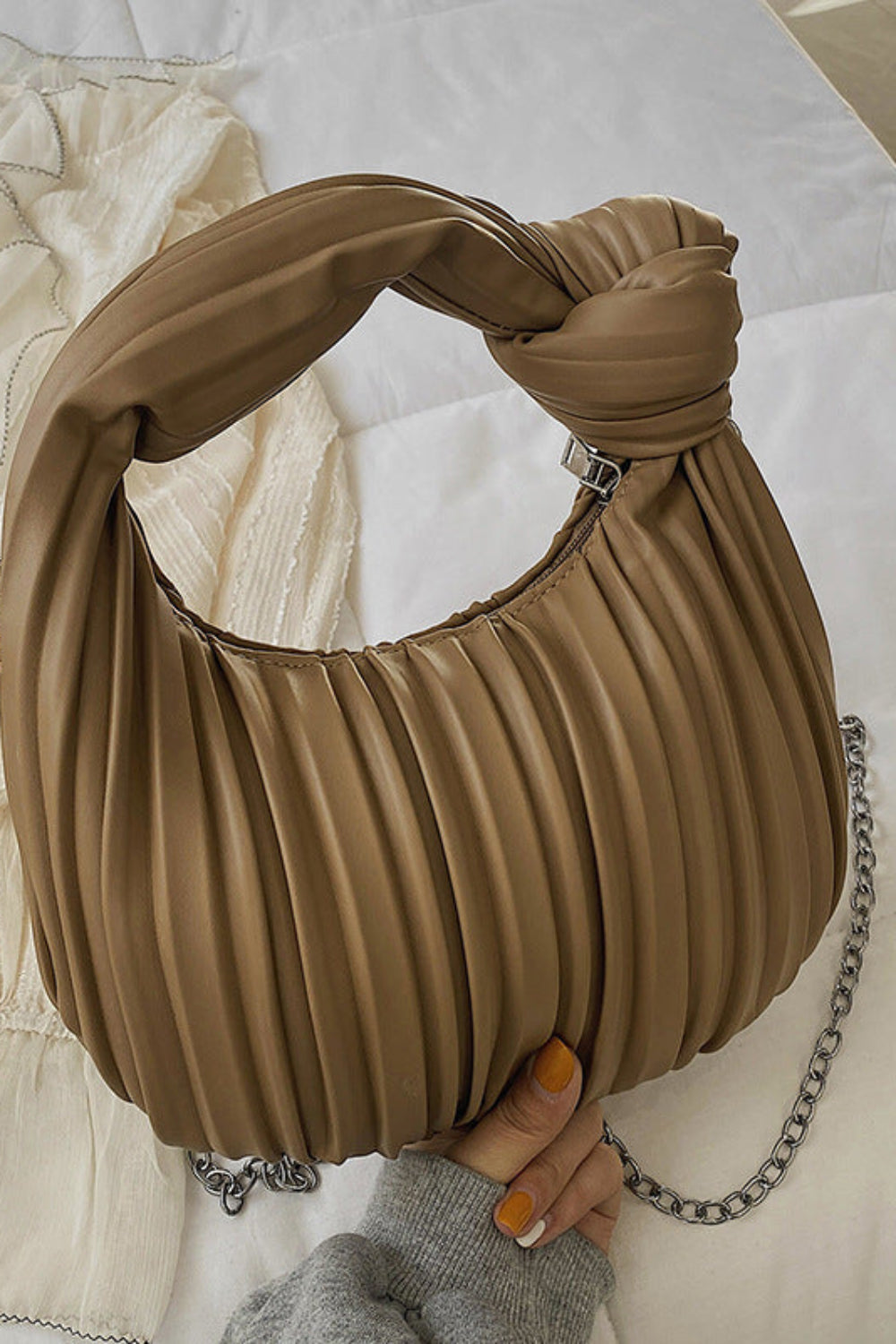 Brown pleated handbag with a chain detail held by a hand on a light background