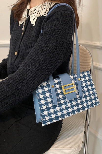 Person holding a blue and white patterned handbag with a gold clasp.