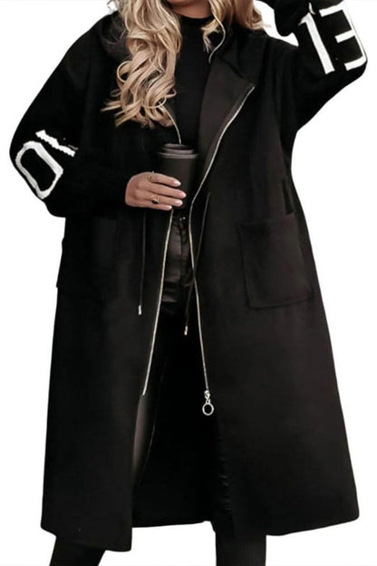 Person wearing a black coat with white lettering on sleeves, holding a coffee cup.