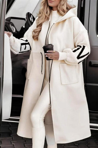 Woman in a long white coat stepping out of a car, holding a coffee cup.