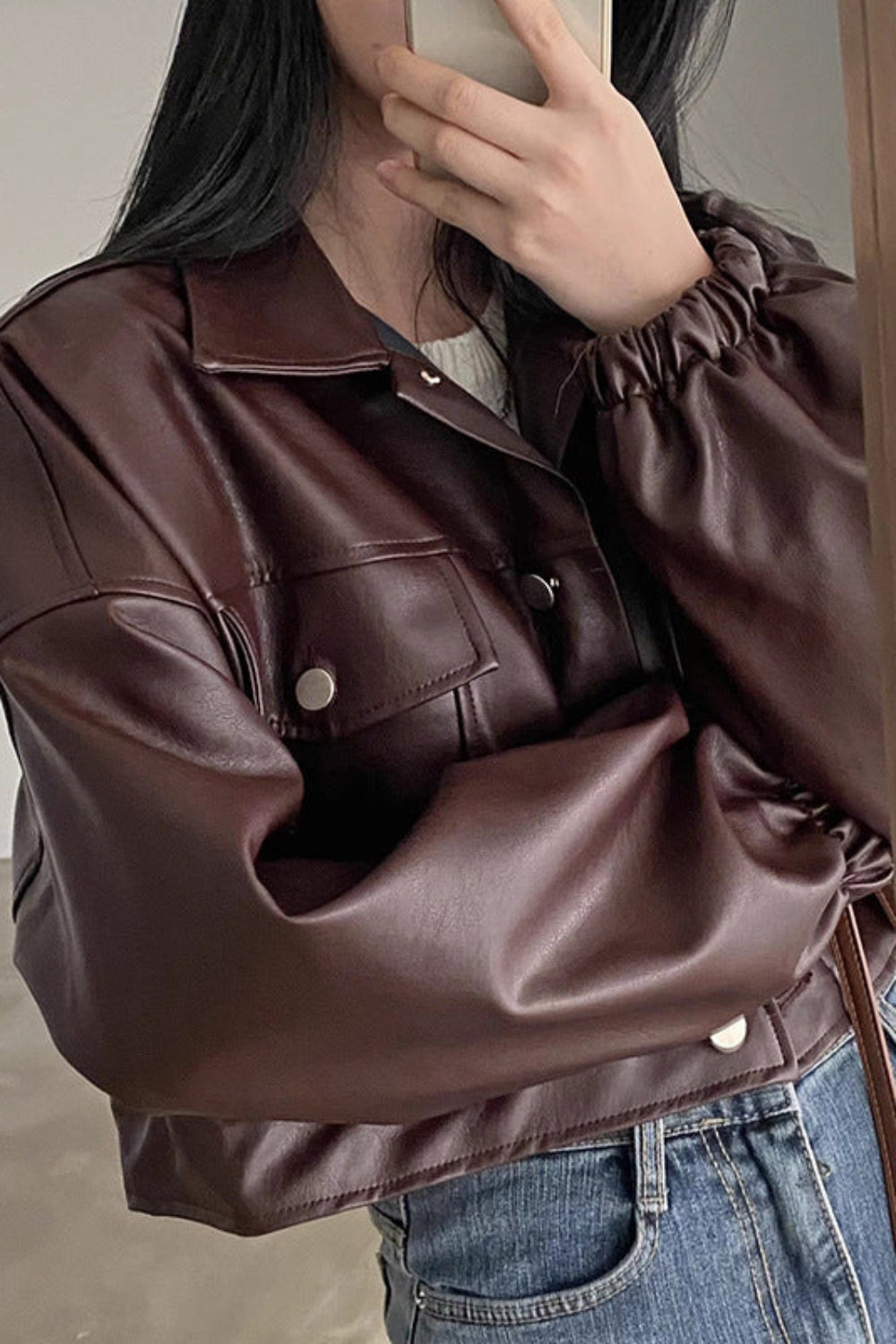 Person wearing a brown leather jacket and blue jeans indoors.