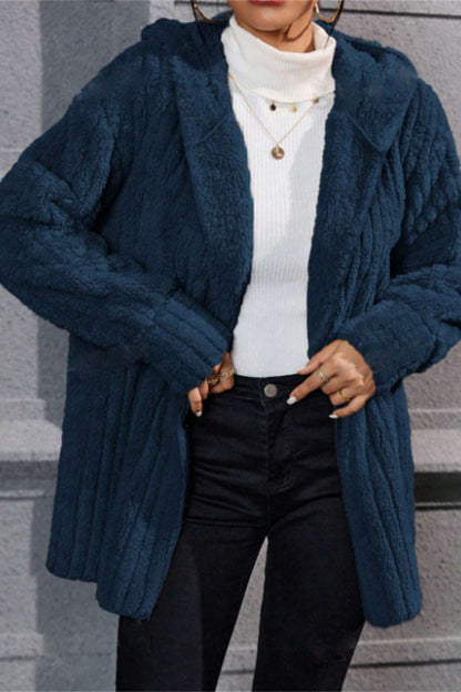 Person wearing a blue knitted cardigan over a white sweater and black pants, standing on steps.