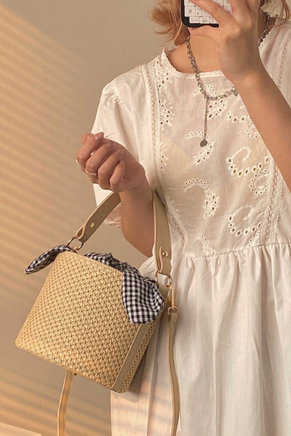 Woman in a white dress holding a straw bag with a checkered lining.