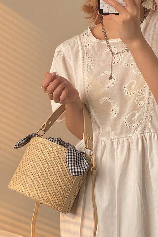 Woman in a white dress holding a straw bag with a checkered lining.