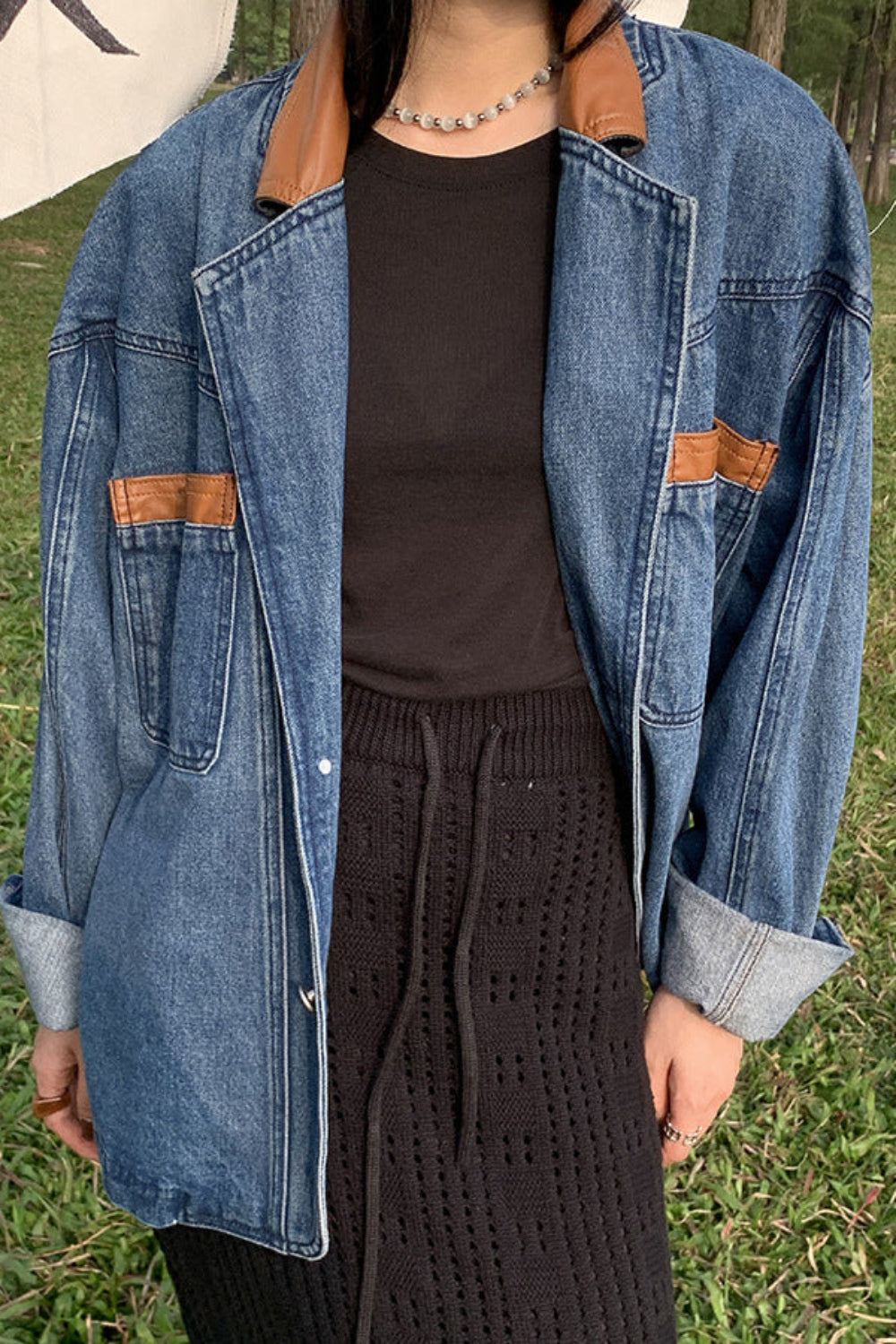 Person wearing a denim jacket with brown accents on a grassy background