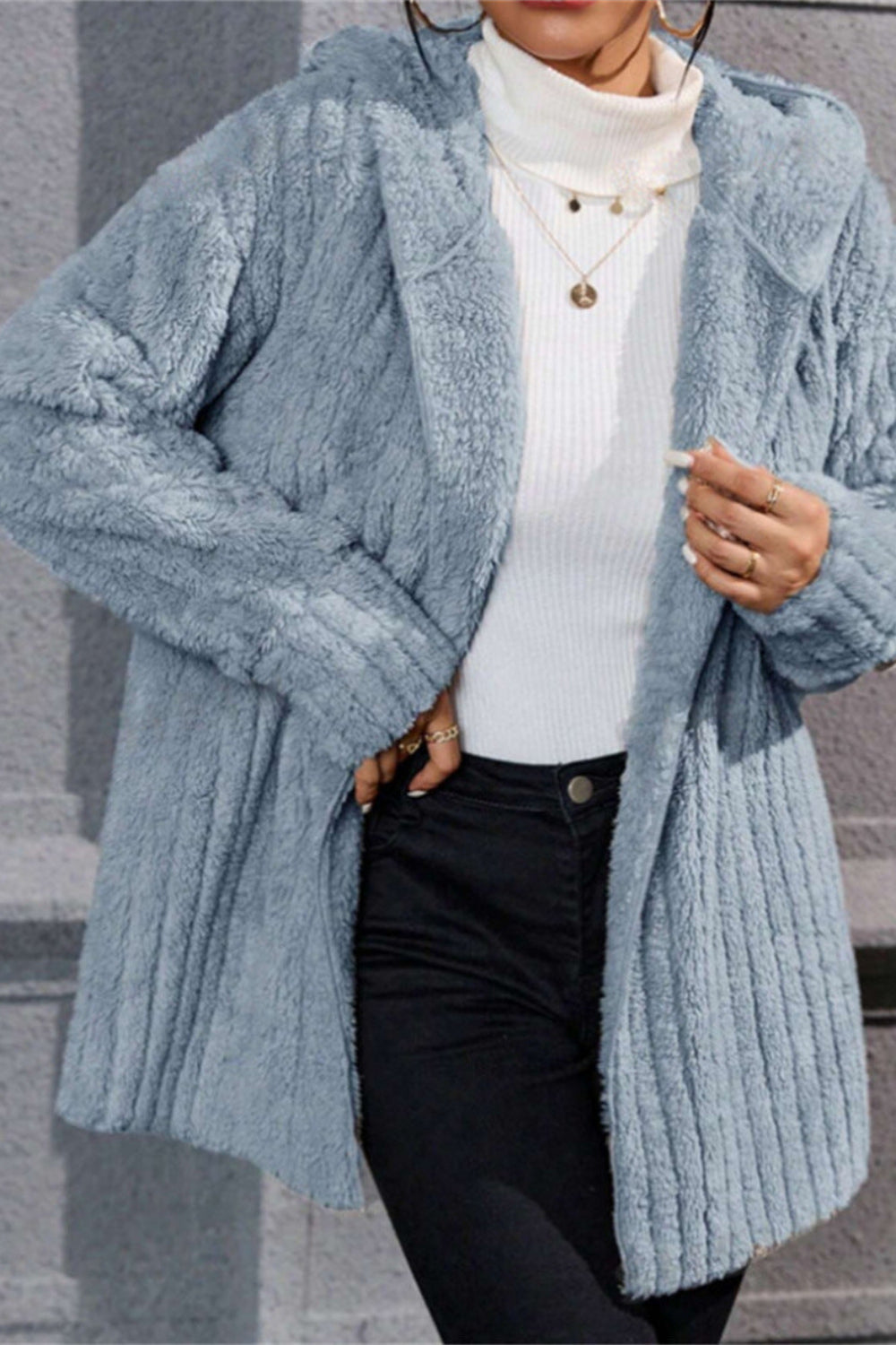 Person wearing a light blue knitted cardigan over a white sweater and black pants.