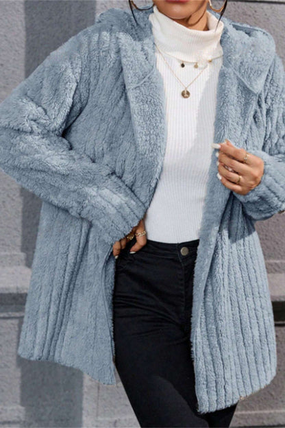 Person wearing a light blue knitted cardigan over a white sweater and black pants.