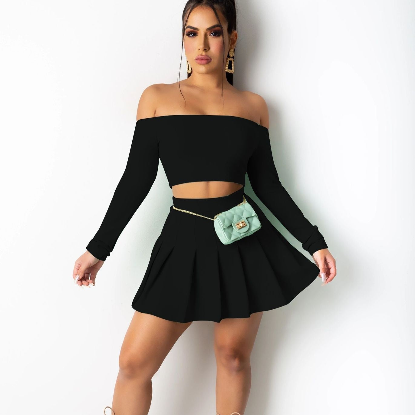 Woman wearing a black off-shoulder top and skirt with a green purse against a white background