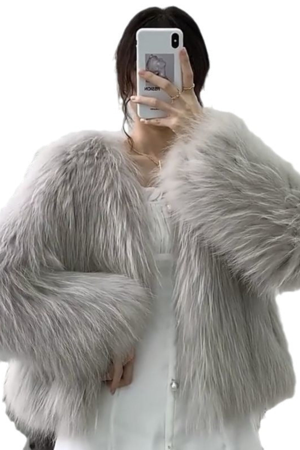 Person wearing a fluffy gray jacket taking a selfie on a white background